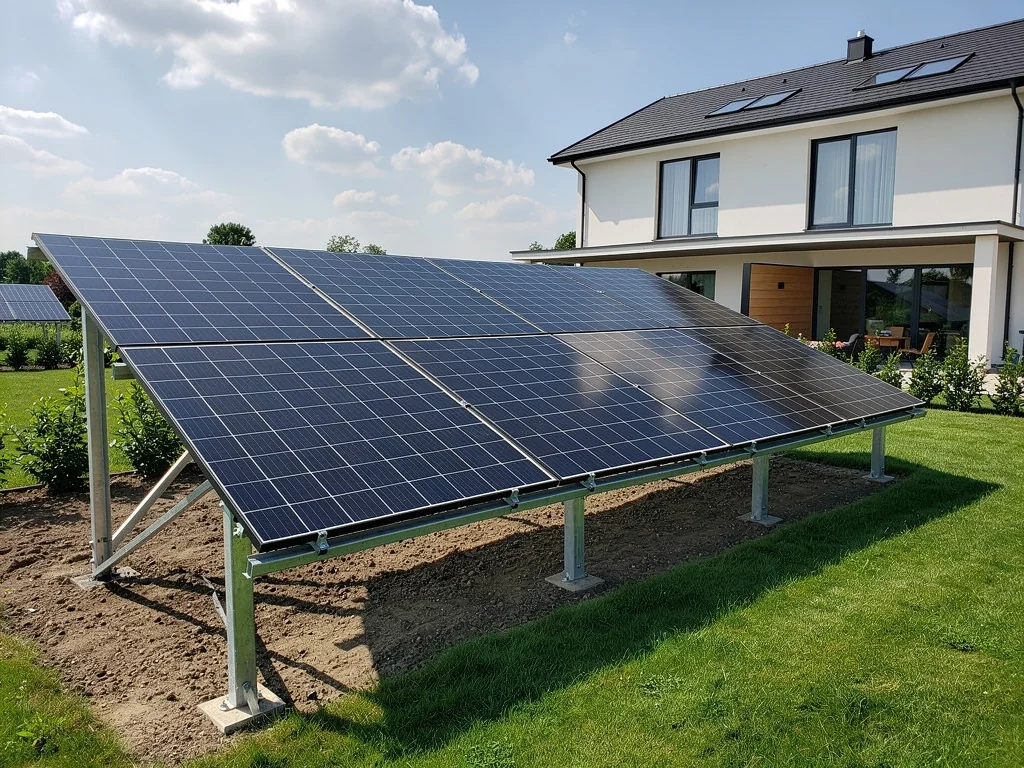 Panneaux solaires installés au sol sur un terrain dégagé, à côté d'un pavillon